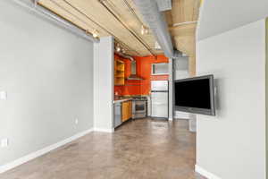 Kitchen with finished concrete floors, stainless steel appliances, wall chimney range hood, and open shelves
