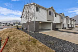 View of side of property with a residential view, brick siding, driveway, a yard, and an attached garage
