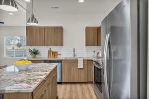 Kitchen with stainless steel appliances, backsplash, light stone counters, brown cabinets, and recessed lighting