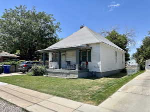 View of front facade featuring covered porch, a shingled roof, a front lawn, and driveway