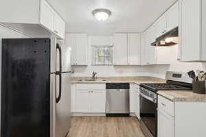 Kitchen with appliances with stainless steel finishes, a textured ceiling, under cabinet range hood, white cabinets, and light countertops