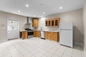 Kitchen with appliances with stainless steel finishes, light countertops, recessed lighting, wall chimney range hood, and glass insert cabinets