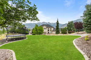 View of grassy yard featuring a trampoline and a mountain view