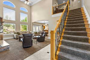 Tiled living area featuring a ceiling fan, arched walkways, stairway, ornamental molding, and a high ceiling