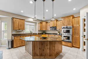 Kitchen featuring appliances with stainless steel finishes, a kitchen island, hanging light fixtures, light tile patterned flooring, and dark stone countertops