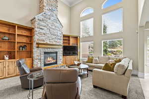 Living area featuring a high ceiling, a stone fireplace, and crown molding
