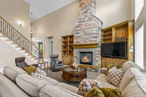 Carpeted living area with a towering ceiling, stairs, a fireplace, crown molding, and a chandelier