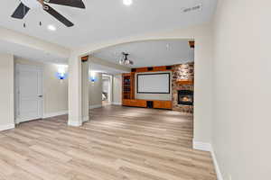 Unfurnished living room with a ceiling fan, light wood-style flooring, recessed lighting, a stone fireplace, and arched walkways