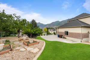 View of green lawn featuring a garden, a mountain view, and a patio area
