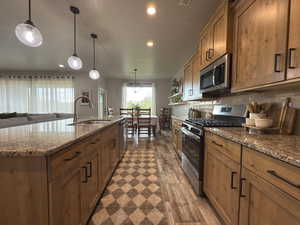 Kitchen with appliances with stainless steel finishes, recessed lighting, dark wood-style flooring, brown cabinetry, and an island with sink