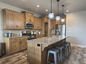 Kitchen featuring wood finished floors, appliances with stainless steel finishes, tasteful backsplash, brown cabinets, and recessed lighting