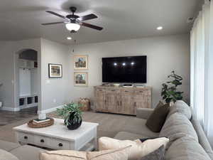 Carpeted living room featuring a ceiling fan, arched walkways, and recessed lighting