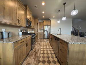Kitchen featuring appliances with stainless steel finishes, tasteful backsplash, wood finished floors, recessed lighting, and a kitchen island with sink