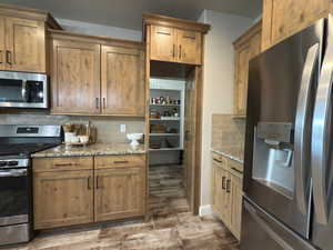Kitchen with appliances with stainless steel finishes, wood finished floors, light stone counters, and decorative backsplash