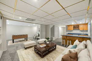 Carpeted living area featuring wet bar, recessed lighting, and a drop ceiling
