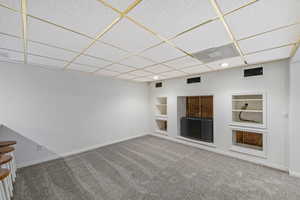 Unfurnished living room featuring built in shelves, a drop ceiling, carpet, and recessed lighting