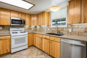 Kitchen featuring stainless steel appliances, light tile patterned floors, decorative backsplash, and light stone counters