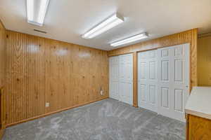 Unfurnished bedroom featuring wood walls, a textured ceiling, two closets, and carpet
