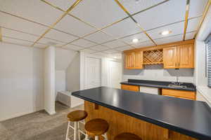Kitchen featuring a paneled ceiling, a kitchen bar, dark countertops, carpet flooring, and white dishwasher