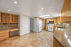 Kitchen featuring tasteful backsplash, white appliances, built in desk, recessed lighting, and light tile patterned floors