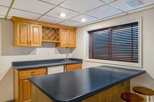 Kitchen with a paneled ceiling, dark countertops, a kitchen bar, and white dishwasher