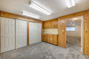 Kitchen featuring a textured ceiling, light colored carpet, brown cabinets, light countertops, and wooden walls