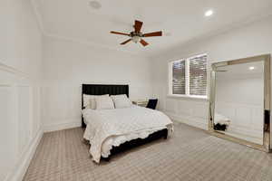 Bedroom featuring a decorative wall, a wainscoted wall, crown molding, light carpet, and ceiling fan