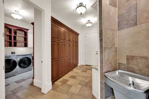 Bathroom with washer and clothes dryer, ornamental molding, tile walls, and stone finish floors