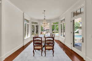Dining space with crown molding, a chandelier, dark wood-style flooring, and plenty of natural light