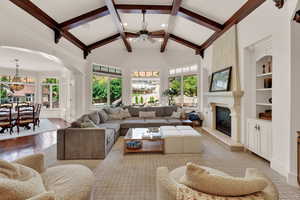 Living room with a ceiling fan, beam ceiling, built in shelves, a fireplace, and arched walkways