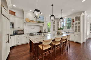 Kitchen featuring tasteful backsplash, ornamental molding, dark wood-type flooring, recessed lighting, and a kitchen island with sink
