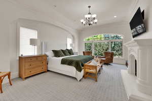 Bedroom with a chandelier, ornamental molding, light carpet, a fireplace with raised hearth, and recessed lighting
