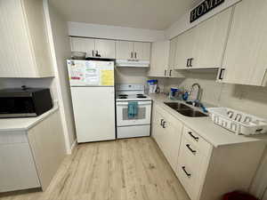 Kitchen with white appliances, light countertops, light wood finished floors, and tasteful backsplash