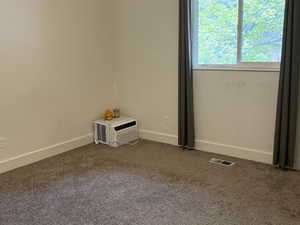 Carpeted empty room featuring baseboards and an AC wall unit