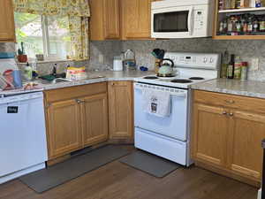 Kitchen with white appliances, dark wood-type flooring, light countertops, backsplash, and brown cabinetry