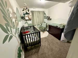 Bedroom featuring a nursery area, a textured ceiling, and carpet flooring