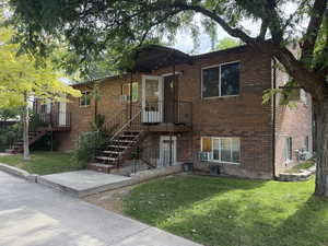 View of front of Triplex with brick siding, a front yard, and stairway