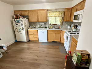 Kitchen with white appliances, light countertops, light wood finished floors, and decorative backsplash