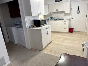 Kitchen featuring light countertops, decorative backsplash, washing machine and dryer, stainless steel microwave, and white cabinetry