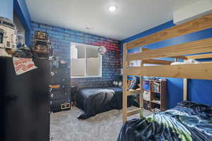 Bedroom with a textured ceiling, carpet floors, and brick wall