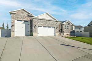 Craftsman-style home featuring a garage, concrete driveway, stone siding, and a gate