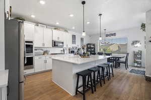 Kitchen with stainless steel appliances, a kitchen breakfast bar, light wood finished floors, white cabinetry, and a chandelier