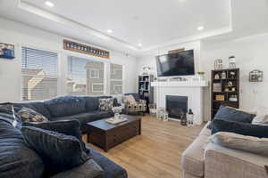 Living room featuring a tray ceiling, light wood-type flooring, recessed lighting, and a fireplace