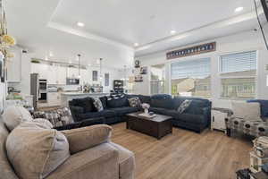 Living area featuring light wood-type flooring, a raised ceiling, and recessed lighting