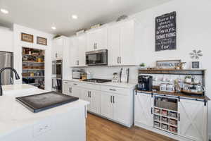 Kitchen featuring light wood-style flooring, white cabinets, stainless steel appliances, and recessed lighting