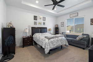 Bedroom with a tray ceiling, light colored carpet, recessed lighting, and ceiling fan
