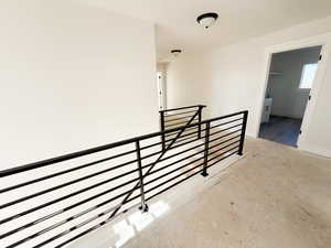 Hallway featuring an upstairs landing and unfinished concrete floors