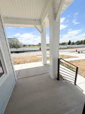 Covered front porch featuring robust white columns, light blue siding, a concrete surface, and a modern black metal railing