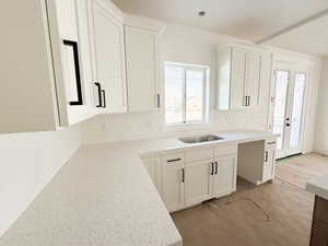 Kitchen featuring light stone counters, white cabinetry, and wood finished floors