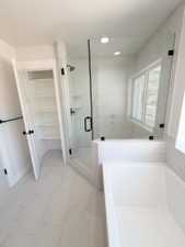 Contemporary bathroom featuring a frameless glass shower enclosure with matte black hardware, a built-in soaking tub, and a spacious linen closet with shelving